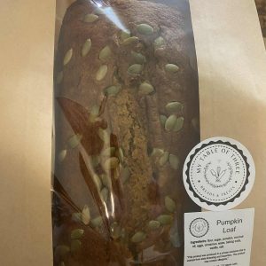 A pumpkin bread loaf with pumpkin seeds on top in a brown paper bag with My Table of Three Business labels on them.