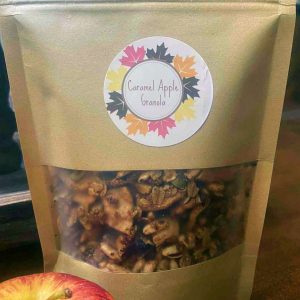 A brown bag of granola with a label on it saying "Caramel Apple Granola". This is a My Table of Three product.