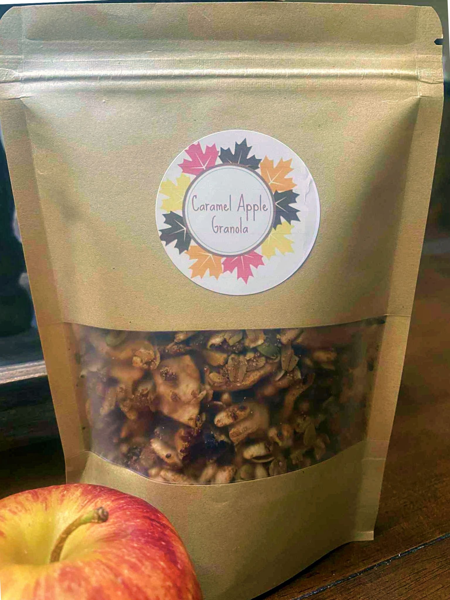 A brown bag of granola with a label on it saying "Caramel Apple Granola". This is a My Table of Three product.